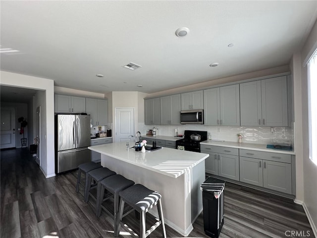 kitchen featuring sink, a center island with sink, gray cabinets, and appliances with stainless steel finishes