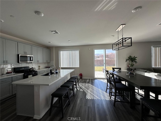 kitchen with sink, dark hardwood / wood-style flooring, hanging light fixtures, a center island with sink, and black range oven