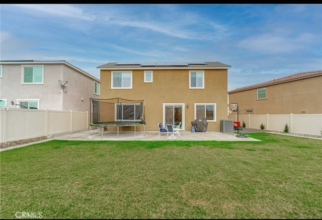 rear view of property featuring a trampoline, a yard, central AC, a patio area, and solar panels