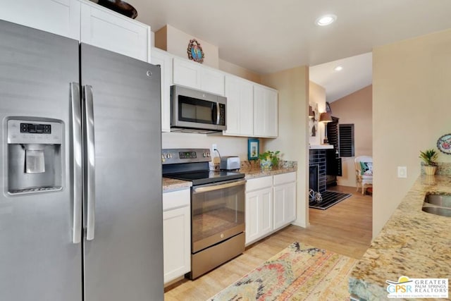 kitchen with light stone countertops, stainless steel appliances, lofted ceiling, light wood-type flooring, and white cabinetry