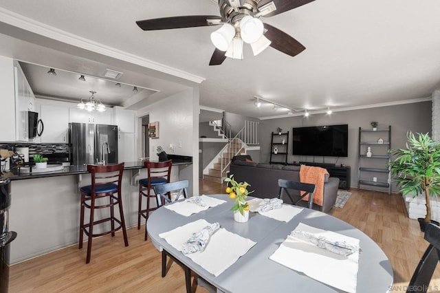 dining space with light hardwood / wood-style floors, track lighting, ornamental molding, and ceiling fan with notable chandelier