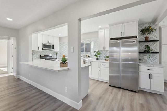 kitchen with white cabinets, appliances with stainless steel finishes, backsplash, and light hardwood / wood-style flooring