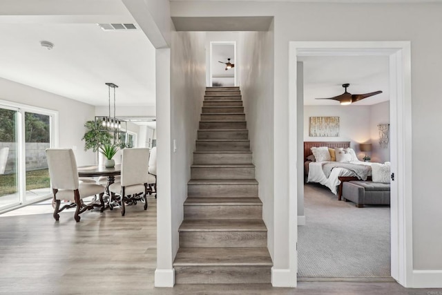 staircase with ceiling fan with notable chandelier and carpet