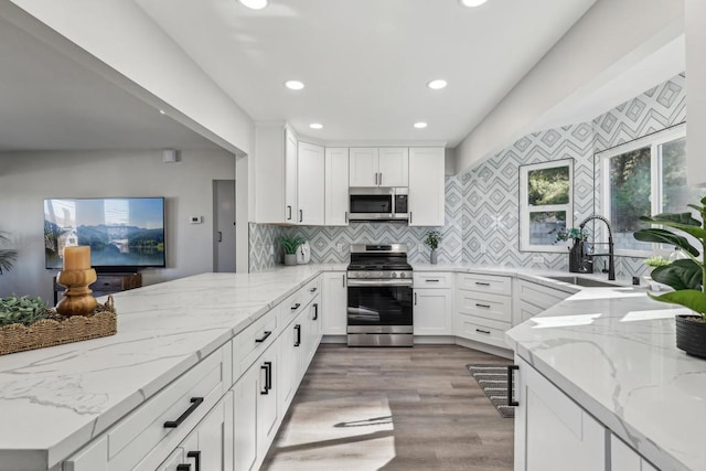 kitchen featuring light stone counters, stainless steel appliances, white cabinetry, and sink