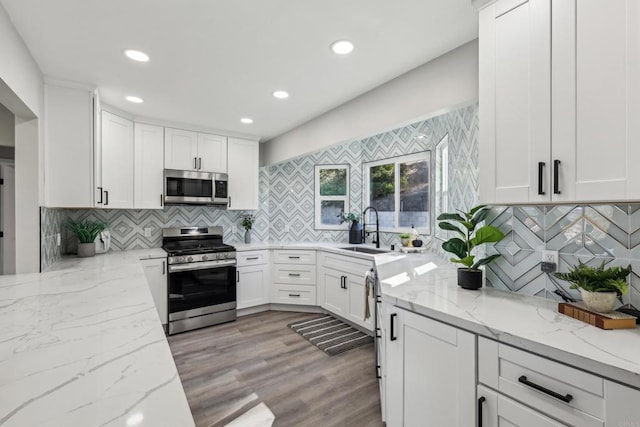 kitchen featuring stainless steel appliances, white cabinets, sink, and light stone countertops