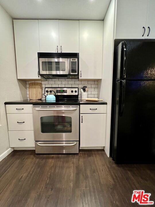 kitchen with stainless steel appliances, white cabinets, backsplash, and dark wood-type flooring