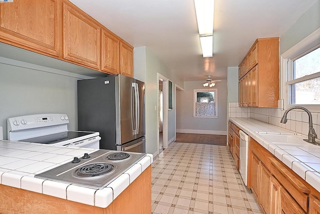 kitchen with white appliances, ceiling fan, tile countertops, and sink