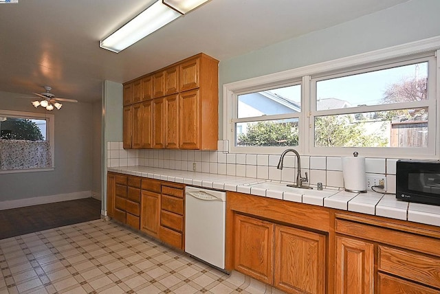 kitchen with white dishwasher, ceiling fan, tile countertops, sink, and tasteful backsplash