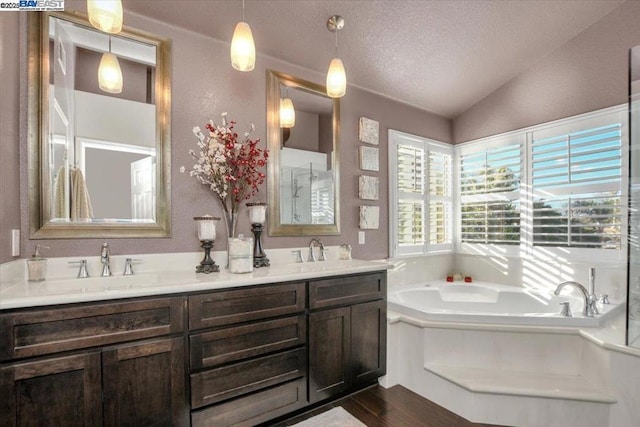 bathroom with hardwood / wood-style floors, a tub, lofted ceiling, vanity, and a textured ceiling