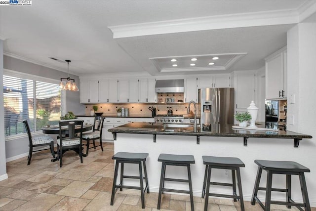 kitchen with wall chimney range hood, sink, stainless steel fridge, a tray ceiling, and white cabinets