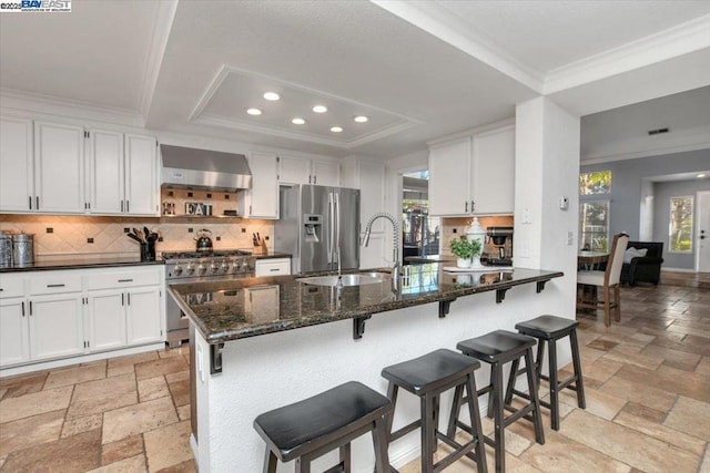 kitchen with white cabinetry, wall chimney range hood, stainless steel appliances, and a raised ceiling