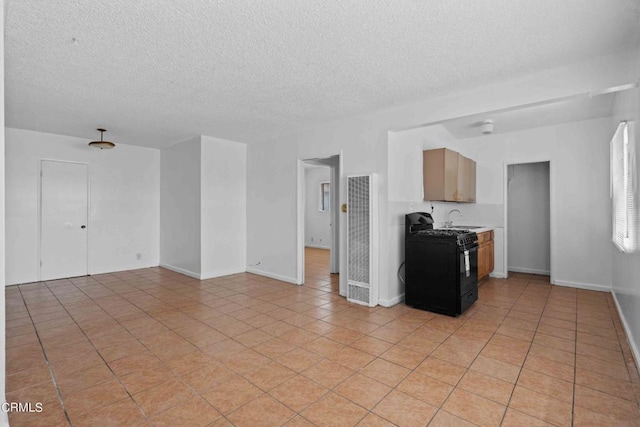 interior space featuring light tile patterned floors, black gas stove, a textured ceiling, and sink