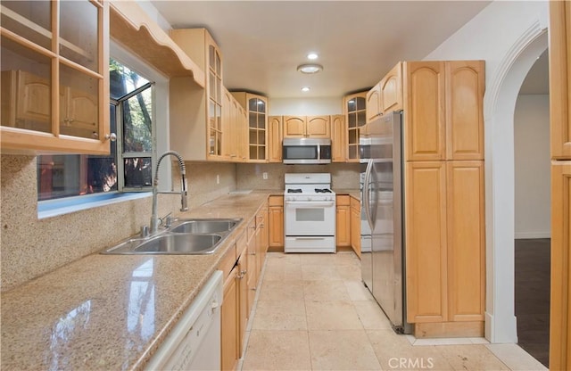 kitchen with stainless steel appliances, light stone countertops, light brown cabinetry, decorative backsplash, and sink