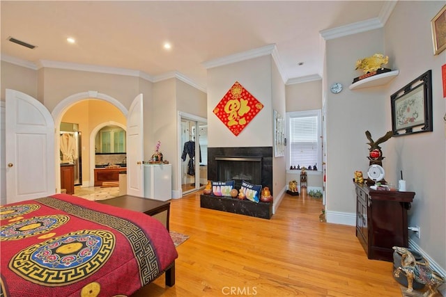 bedroom with a multi sided fireplace, ensuite bathroom, crown molding, and light hardwood / wood-style flooring