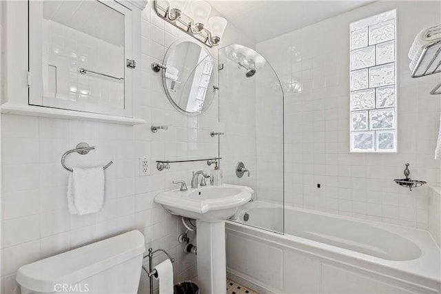 bathroom with toilet, tiled shower / bath combo, and tile walls