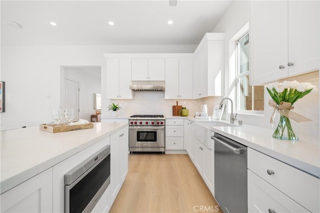 kitchen with sink, white cabinetry, light wood-type flooring, backsplash, and appliances with stainless steel finishes