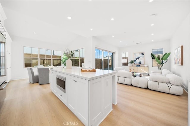 kitchen featuring vaulted ceiling, a center island, light hardwood / wood-style floors, wall oven, and white cabinets