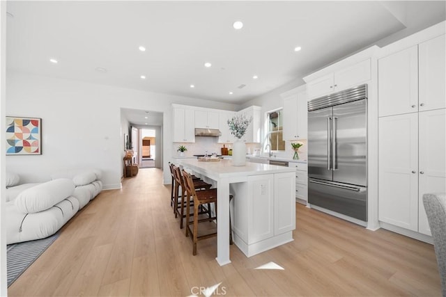 kitchen with a center island, light hardwood / wood-style floors, white cabinetry, stainless steel built in refrigerator, and a kitchen breakfast bar