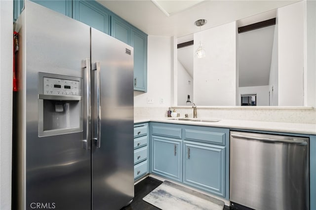 kitchen with appliances with stainless steel finishes, hanging light fixtures, blue cabinetry, and sink