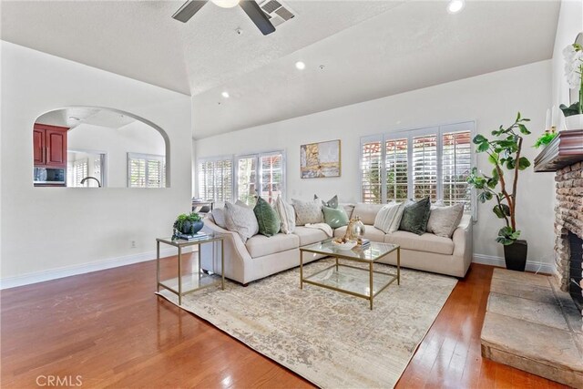 living room featuring a stone fireplace, dark wood-type flooring, lofted ceiling, and ceiling fan