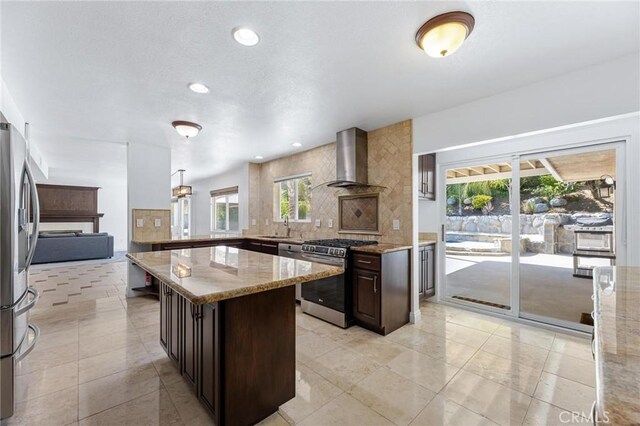 kitchen featuring pendant lighting, wall chimney range hood, sink, stainless steel appliances, and light stone countertops