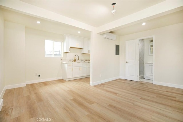 unfurnished living room featuring electric panel, light hardwood / wood-style floors, sink, and a wall unit AC