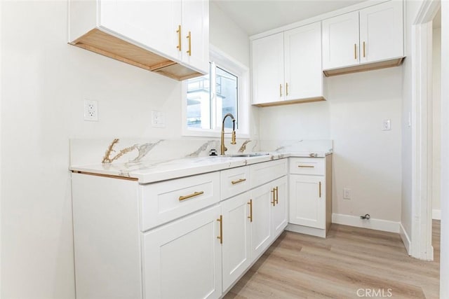 kitchen featuring white cabinets, light stone countertops, light hardwood / wood-style floors, and sink