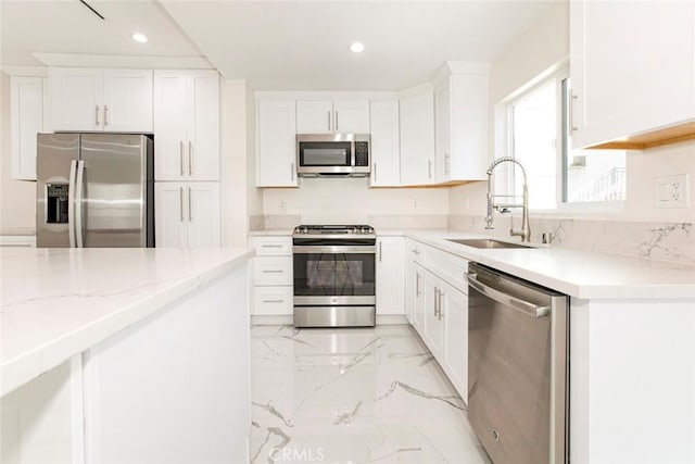 kitchen with light stone countertops, appliances with stainless steel finishes, white cabinetry, and sink