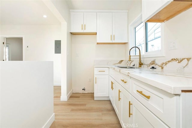 kitchen featuring sink, white cabinetry, light wood-type flooring, and electric panel