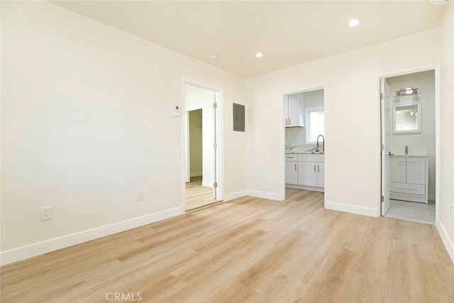 unfurnished bedroom with sink, light wood-type flooring, electric panel, and connected bathroom