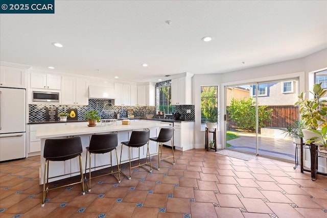 kitchen with a breakfast bar area, built in appliances, and white cabinetry