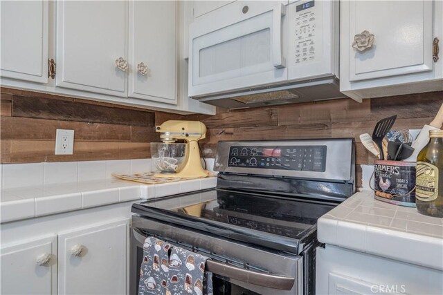 kitchen featuring white cabinetry, wooden walls, stainless steel range with electric stovetop, and tile counters