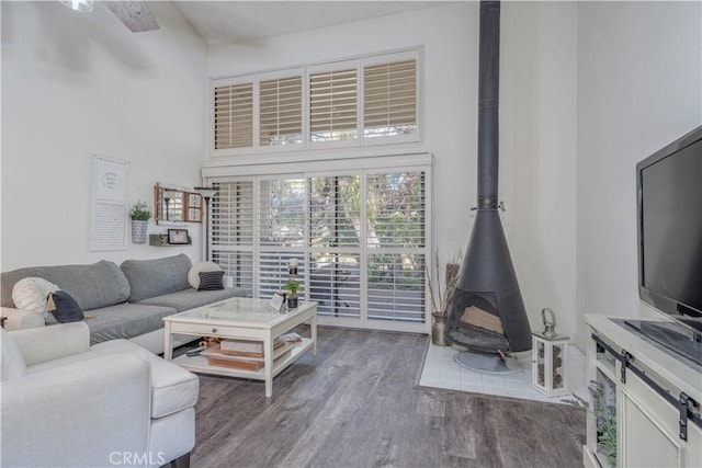 living room with a high ceiling, wood finished floors, and a wood stove