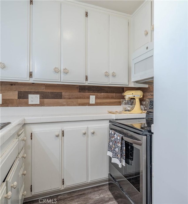 kitchen with white microwave, tile counters, decorative backsplash, stainless steel range with electric cooktop, and white cabinets