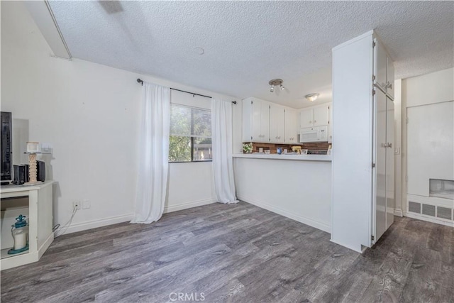 kitchen with white microwave, visible vents, light countertops, dark wood-style floors, and white cabinetry