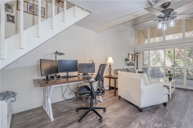 office area featuring a ceiling fan, a textured ceiling, wood finished floors, baseboards, and a towering ceiling