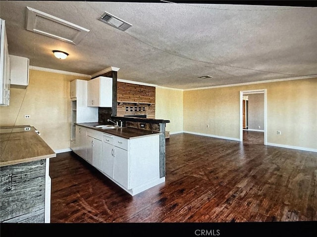 kitchen featuring white cabinetry, kitchen peninsula, dark wood-type flooring, ornamental molding, and sink