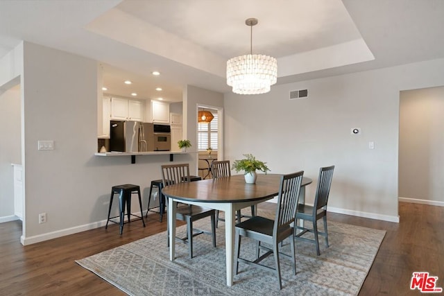 dining area featuring a raised ceiling, dark hardwood / wood-style flooring, and an inviting chandelier