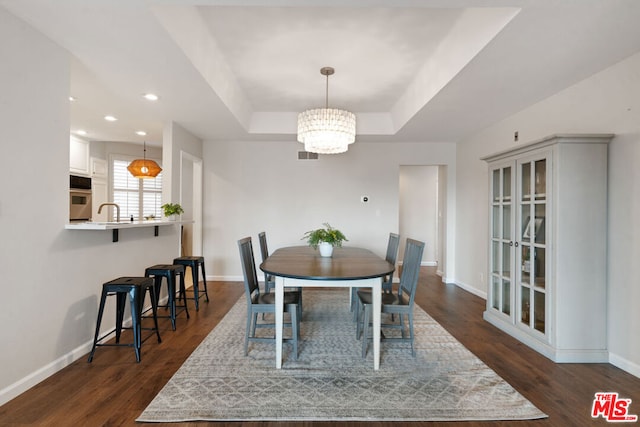 dining room with a notable chandelier, dark hardwood / wood-style flooring, sink, and a tray ceiling