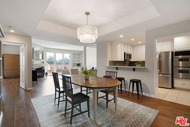 dining space featuring light wood-type flooring, a tray ceiling, a chandelier, and sink