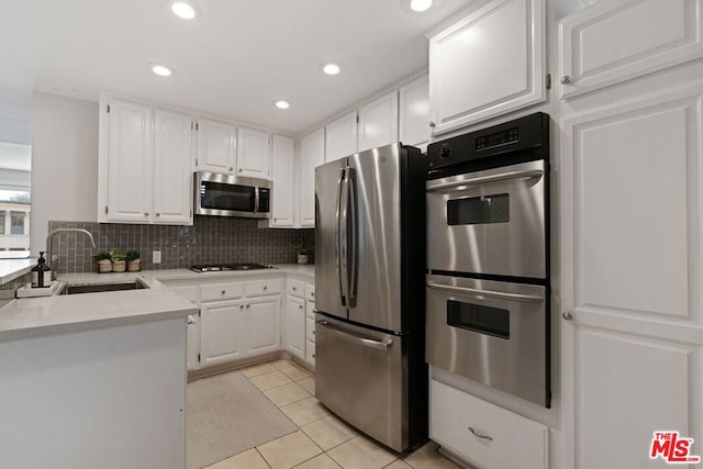 kitchen featuring appliances with stainless steel finishes, light tile patterned floors, white cabinets, backsplash, and sink