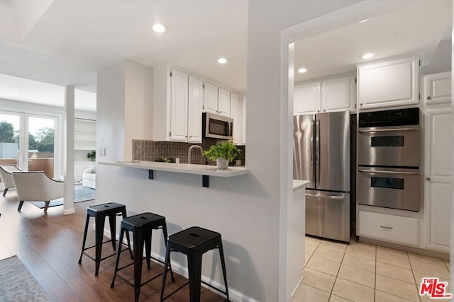 kitchen featuring a kitchen breakfast bar, stainless steel appliances, kitchen peninsula, white cabinets, and sink