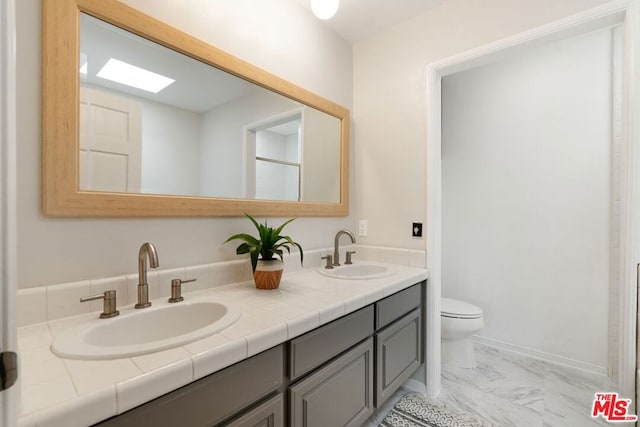 bathroom with toilet, vanity, and a skylight