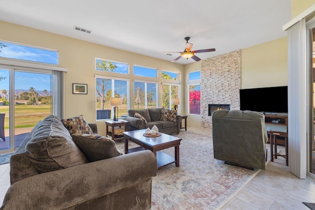 living room with ceiling fan, a stone fireplace, and light tile patterned flooring