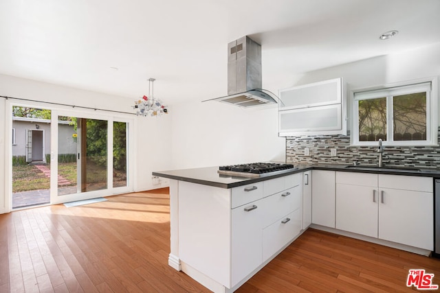 kitchen with island exhaust hood, stainless steel gas cooktop, backsplash, white cabinetry, and sink