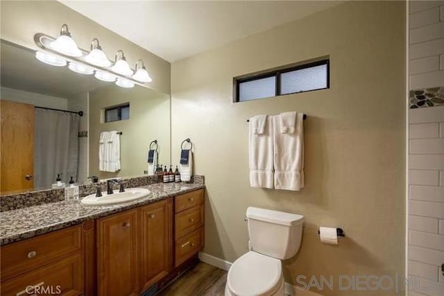 bathroom with toilet, vanity, hardwood / wood-style flooring, and curtained shower