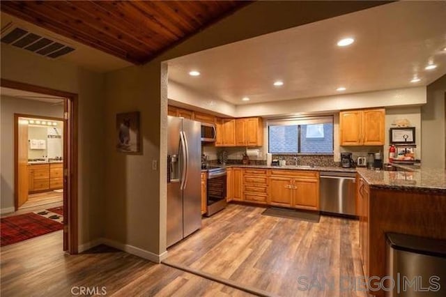 kitchen with stainless steel appliances, hardwood / wood-style flooring, kitchen peninsula, dark stone counters, and wood ceiling