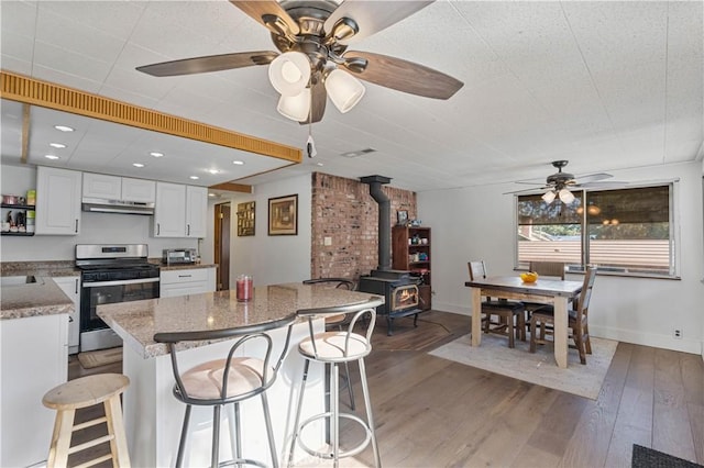 kitchen with light hardwood / wood-style floors, white cabinetry, stainless steel range oven, a kitchen breakfast bar, and a wood stove