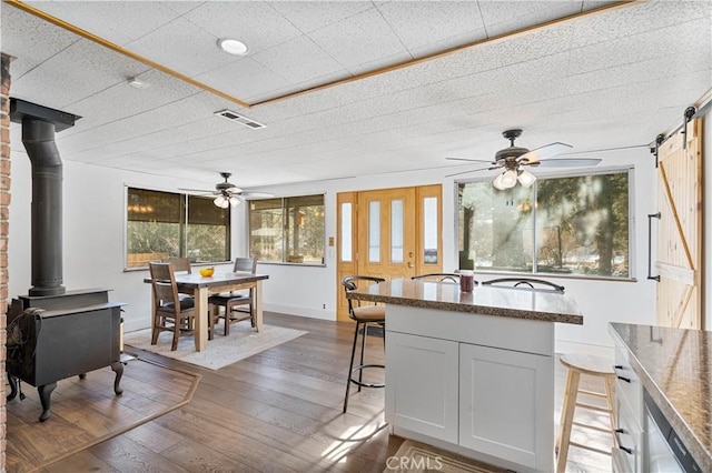 kitchen featuring white cabinetry, hardwood / wood-style floors, ceiling fan, a wood stove, and a kitchen breakfast bar