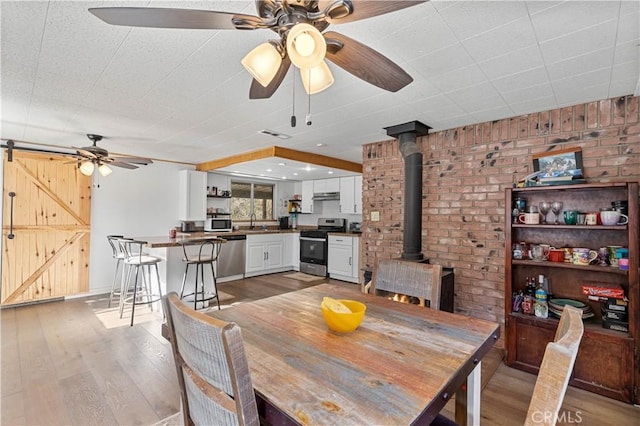 dining room featuring light hardwood / wood-style floors, a wood stove, sink, ceiling fan, and a barn door